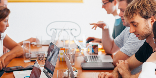 a team of workers in casual clothes in front of their laptops sitting opposite each other