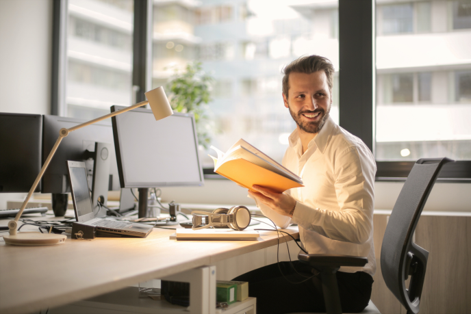 men smiling at the camera sitting at a desk in an brightly lit office